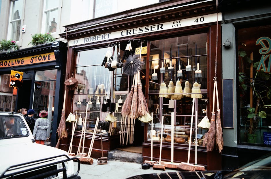 Exterior storefront of a hardware and cleaning supplies shop on Anerley High Street, featuring an array of cleaning tools and materials. In front, various brooms with wooden handles, dustpans, and bru